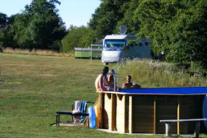 Wohnmobil mit Vorzelt auf einem Campingplatz, im Hintergrund Zelt und Bäume, davor Holzterrasse mit Sitzbank.