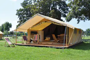 Großes Zelt mit Holzstühlen und Tisch auf einer gepflasterten Fläche, umgeben von Rasen und Bäumen im Campingbereich.