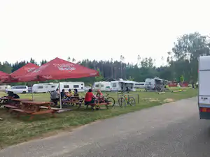Rote Zeltüberdachung auf dem Campingplatz, daneben Wohnmobile, Fahrräder und Picknicktische auf einer Wiese.