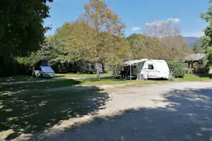 Stellplätze auf einem Campingplatz mit Wohnwagen und Zelt, daneben ein Auto, umgeben von Bäumen und Rasen.