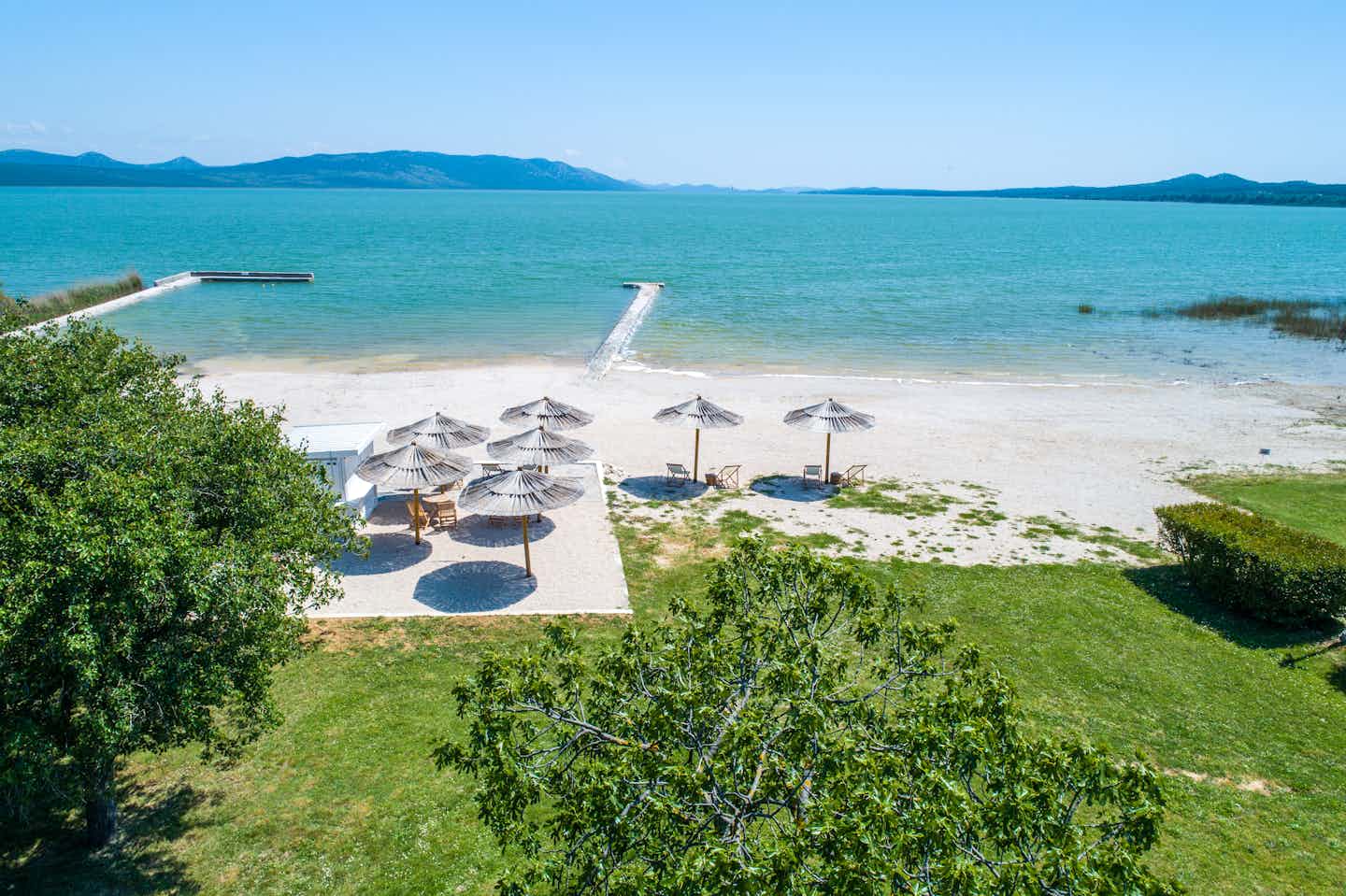 Camp Vransko Jezero Crkvine - der Strand des Campingplatzes mit Liegestühlen und Sonnenschirmen