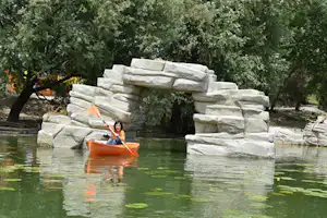 Kajak auf einem ruhigen Fluss vor einer Steinmauer mit großen Felsblöcken und Bäumen im Hintergrund.