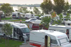 Wohnmobile und Caravans auf einem Campingplatz, im Hintergrund ein Fluss und Bäume zwischen den Stellplätzen.