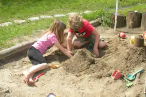 Kinder spielen im Sandkasten, kneten Sand mit Schaufeln und Werkzeugen auf einem Campingplatz.