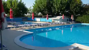 Schwimmbecken mit blauem Wasser und Liegen am Campingplatz, umgeben von Hecken und Sonnenschirmen.