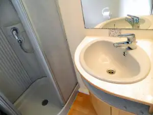 Waschbecken im Badezimmer mit Spiegelschrank, Armatur und Duscheingang mit Duschkopf und Bodenablauf.