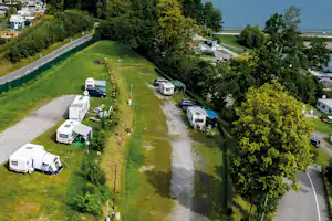Luftaufnahme von Campingstellplätzen mit Wohnmobilen und Zelten auf einer grünen Wiese, entlang einer Straße und Hecken.