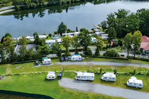 Wohnmobile auf einem Campingplatz am See, umgeben von Bäumen und Rasenflächen mit Wegen zwischen den Stellplätzen.
