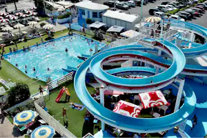 Großer Wasserpark mit mehreren blauen Rutschen, Kinderbecken und Liegen auf dem Campingplatz, daneben Wege und Zäune.