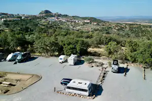 Wohnmobile und Campingfahrzeuge auf einem Stellplatz mit Betonfläche, umgeben von Bäumen und Hügeln, Blick ins Tal.
