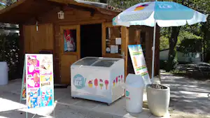 Eiswagen vor einer Holz-Holzhütte mit Werbeplakaten, Eismaschine und Eimer auf dem Campingplatz-Pfad.