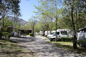 Campingplatz mit Wohnwagen und Wohnmobilen entlang eines breiten Wegs, umgeben von Bäumen und grünen Rasenflächen.