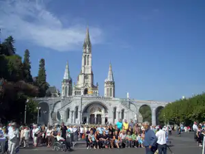 Große Kathedrale mit hohen Türmen und Arkaden am Platz, viele Menschen stehen und gehen im Vordergrund.