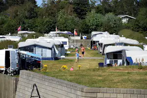 Wohnmobile und Campingbusse auf dem Stellplatz zwischen Hecken, mit Markisen, Fahrrädern und Rasenfläche.