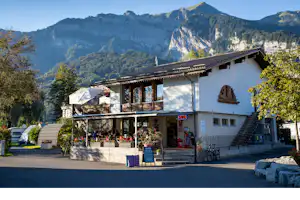Ferienhaus mit Balkon und Terrasse, davor Sitzbank und Fahrräder, im Hintergrund Berge und bewaldete Hänge.