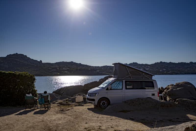 Camping Acapulco - Campingbulli mit daneben sitzenden Campern, die auf das Mittelmeer schauen