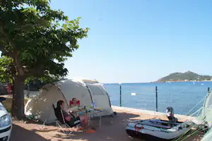 Zelte am Campingplatz am Meer, unter einem Baum, mit Tisch und Stühlen am Strandweg und Blick auf die Bucht.