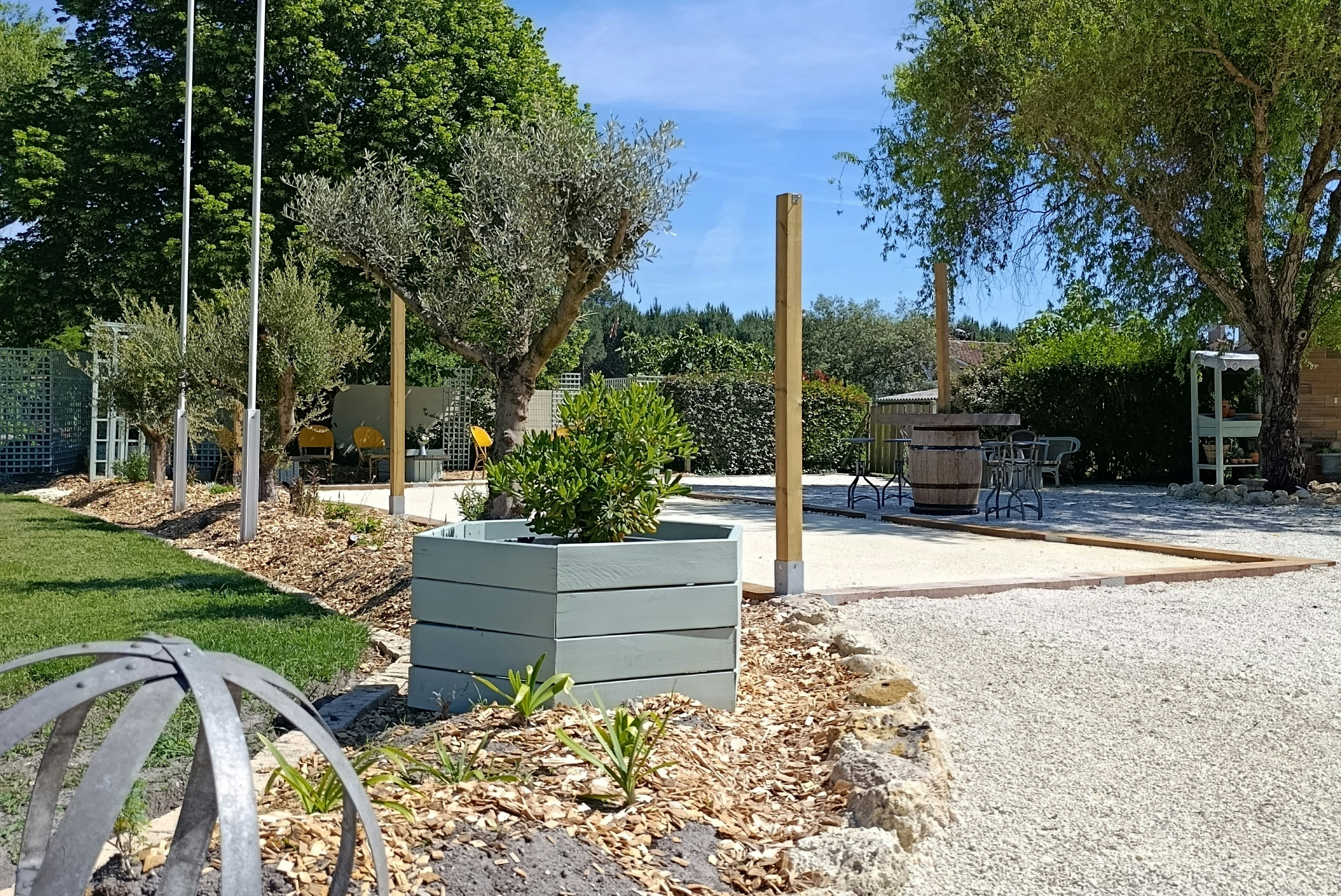 Campingplatz mit Fahnenmast, französischer Flagge, Kiesweg und Sitzbereich im Garten mit Bäumen und Sträuchern.