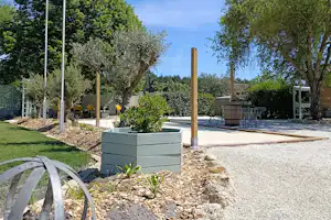 Campingplatz mit Fahnenmast, französischer Flagge, Kiesweg und Sitzbereich im Garten mit Bäumen und Sträuchern.