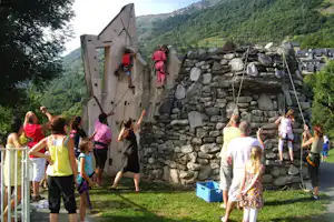 Kletterwand am Campingplatz mit Kindern und Erwachsenen auf dem Rasen, Seile und Steine an der Felswand im Bergtal.