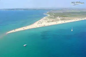 Luftaufnahme einer Küste mit Sandstrand, Booten im Wasser und einer langen Uferstraße entlang der Bucht.