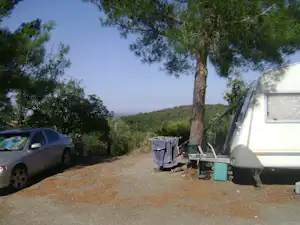 Campingzelt auf einem Kiesplatz neben einem Auto, mit Wäscheleine und Campingausrüstung am Zelt.