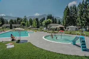 Schwimmbecken mit Liegen und Sonnenschirmen, daneben ein zweites Becken, Campinghäuser und Bäume im Hintergrund.