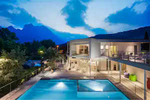 Camping Al Porto - Das Hauptgebäude des Campingplatz mit Swimmingpools und Sitzgelegenheiten, sowie einem Balkon mit Sonnenliegen bei Nacht