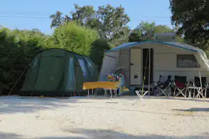 Grünes Zelt und Wohnwagen auf einem Campingplatz, davor Tisch und Stühle unter Markise, umgeben von Bäumen.