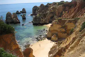 Felsige Küste mit kleinem Sandstrand, türkisfarbenem Meer und Felsformationen entlang der Küste.