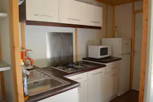 Campingküche mit Herd, Mikrowelle und Spüle, Holzrahmen und Schränken, Wasserkocher und Kaffeemaschine auf der Arbeitsplatte.