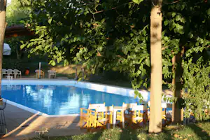 Blauer Camping-Pool mit Holzstühlen am Beckenrand, umgeben von Bäumen und Grün im Hintergrund.