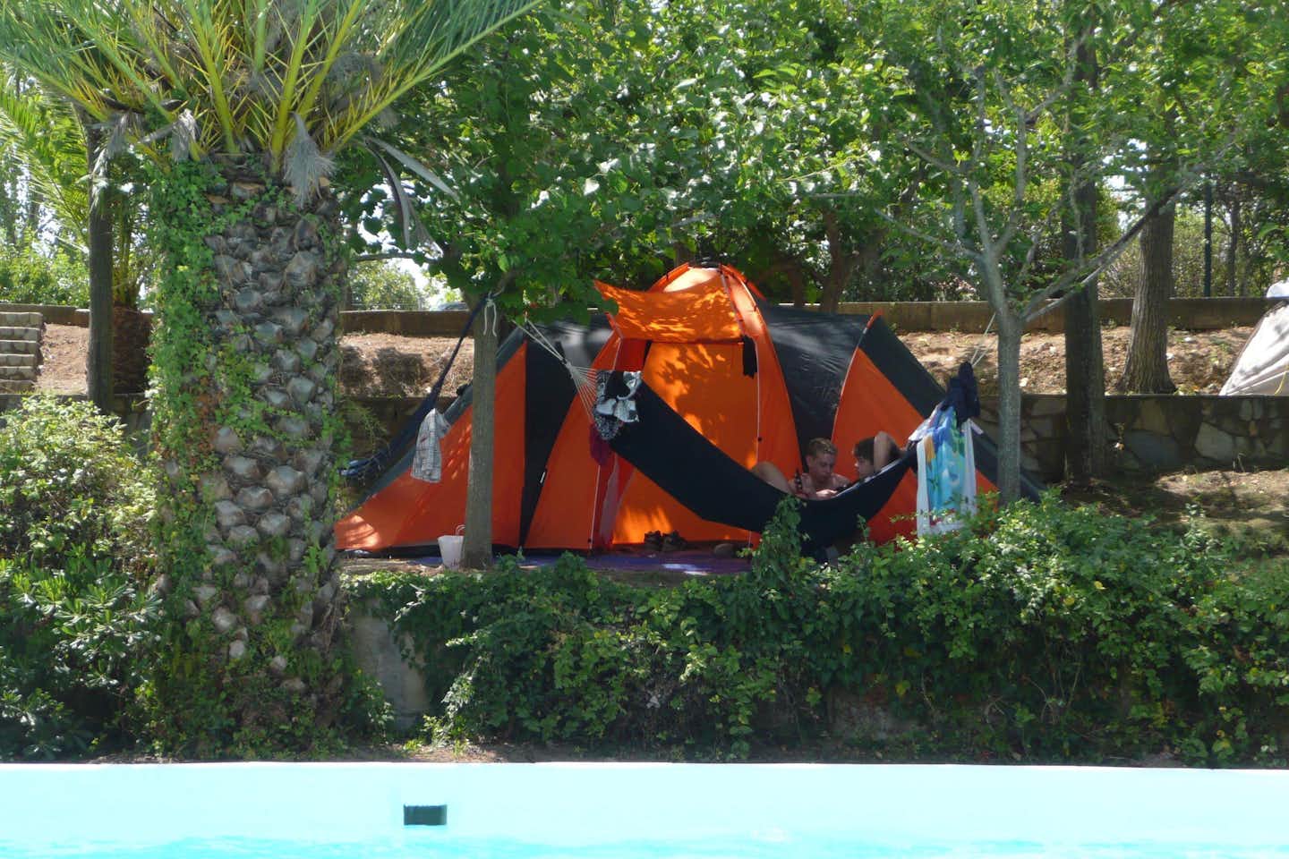 Camping Alphiós - Zelt zwischen Bäumen auf dem Campingplatz mit zwei Campern davor