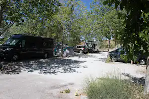 Campingplatz mit Wohnmobilen und Zelt zwischen Bäumen, gepflasterter Stellplatz und Fahrzeuge am Wegesrand.