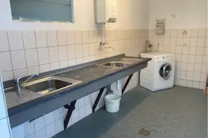 Küchenzeile mit Doppelspüle, Arbeitsplatte und Waschmaschine in einem hell gefliesten Sanitärraum.