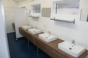 Reihe von Waschbecken in einem hellen Camping-Badezimmer mit Holz-Waschtisch und weißen Fliesen.