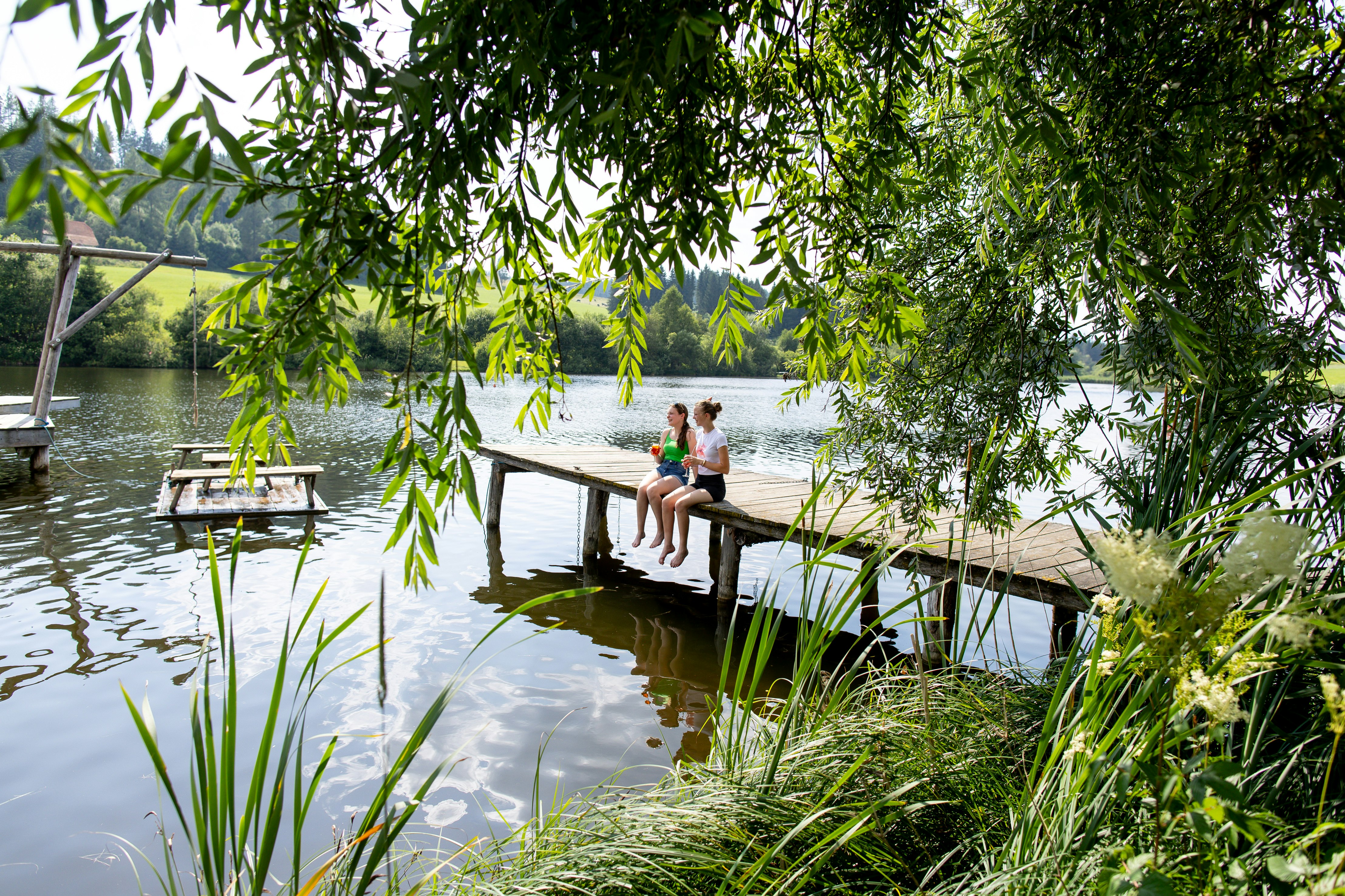 Camping am Badesee - Camperinnen sitzen auf dem Steg am Badestrand