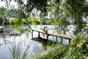 Camping am Badesee - Camperinnen sitzen auf dem Steg am Badestrand