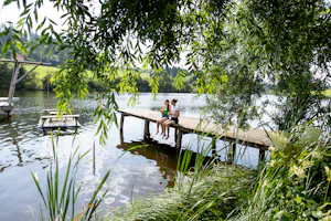 Camping am Badesee - Camperinnen sitzen auf dem Steg am Badestrand