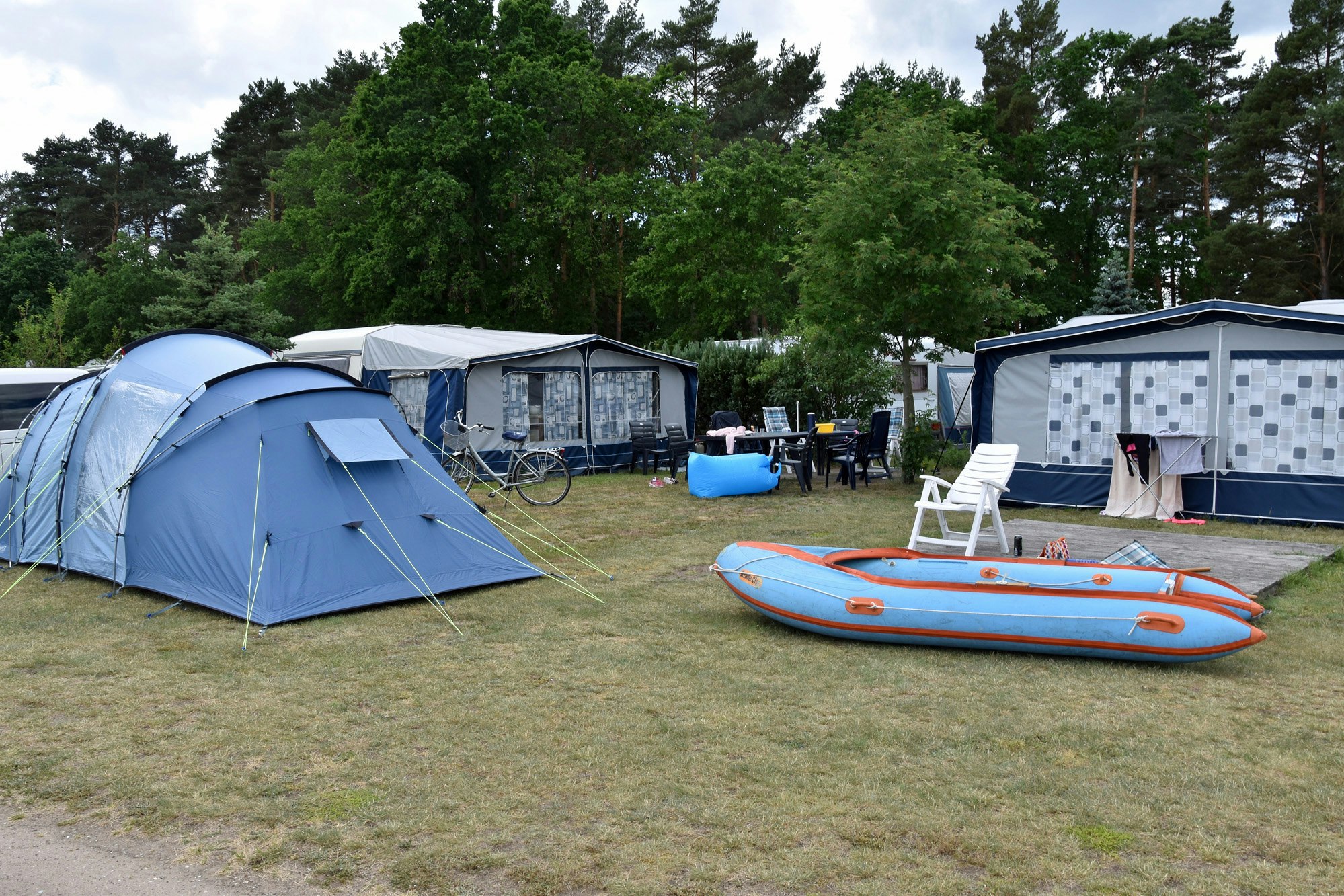 Blaues Zelt auf einem Campingplatz, daneben ein Schlauchboot und Campingstühle vor weiteren Zelten und Wohnwagen.