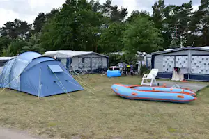 Blaues Zelt auf einem Campingplatz, daneben ein Schlauchboot und Campingstühle vor weiteren Zelten und Wohnwagen.