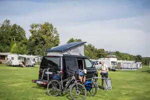 Wohnmobil mit Markise und Fahrrädern auf dem Campingplatz, daneben weitere Wohnmobile und Zelte vor grünen Bäumen.