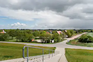 Blick von einer Terrasse auf einen Campingplatz mit Wegen, Rasenflächen und mehreren Häusern im Grünen.