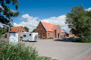 Wohngebäude und Stellplatz mit Wohnwagen auf gepflastertem Weg, umgeben von Bäumen und Sträuchern.