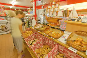 Bäckerei im Campingbereich: Auslage mit Brot und Gebäck in Körben, Zelte im Hintergrund und ein Verkäufer im Vordergrund.