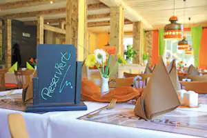 Tischdekoration im Campingzelt: Blumenstrauß in Vase, Platzkarten auf dem Tisch und Servietten, Holzstühle im Hintergrund.