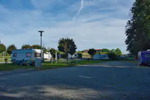 Wohnwagen auf einem Campingplatz, gepflasterter Weg und Rasenflächen, Bäume und Laterne im Hintergrund.