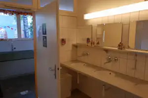 Camping-Badezimmer mit Waschbecken, Armaturen und Fliesenwand, daneben Fenster mit Blick ins Freie.