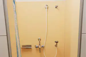 Duschkopf und Armatur in einer gelben Duschkabine, mit Duschschlauch und Wandhalterung.