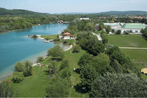 Camping am See - Luftaufnahme auf den See, an dem Der Campingplatz liegt und den Campingplatz im Hintergrund